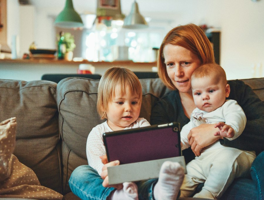 A warm home moment with a caregiver reading on a tablet with two young children
